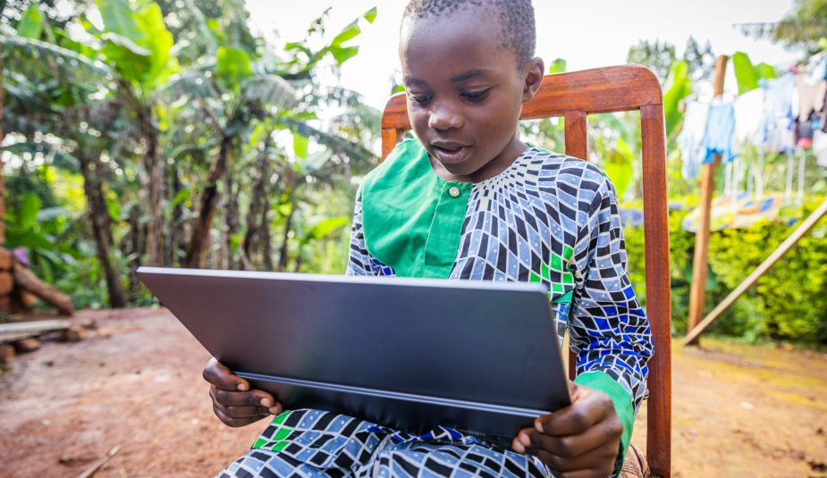 African young student sitting outdoors, keen on his tablet rehearsing his lessons.